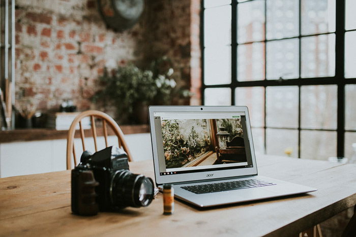 A DSLR camera and laptop on a wooden table 