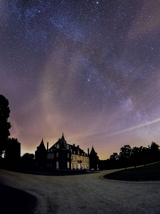 Chateau de la Hulpe in Brussels against a night sky at dusk, lit in blues , oranges, and purples