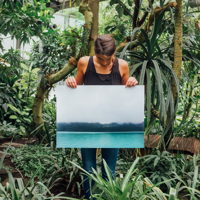 A woman standing in a tropical forest setting holding up a large sized photo print