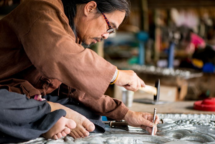 Close up shot of a man in a brown jacket crouched over on the floor working on crafting his sculpture