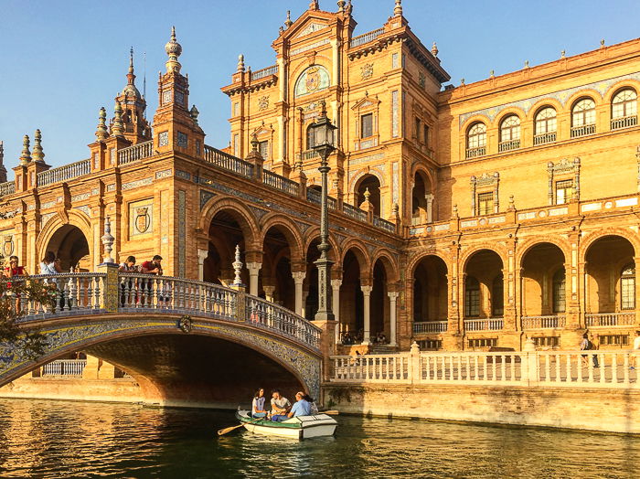 Bright travel photography of people in a boat on a canal in front of a beautiful building