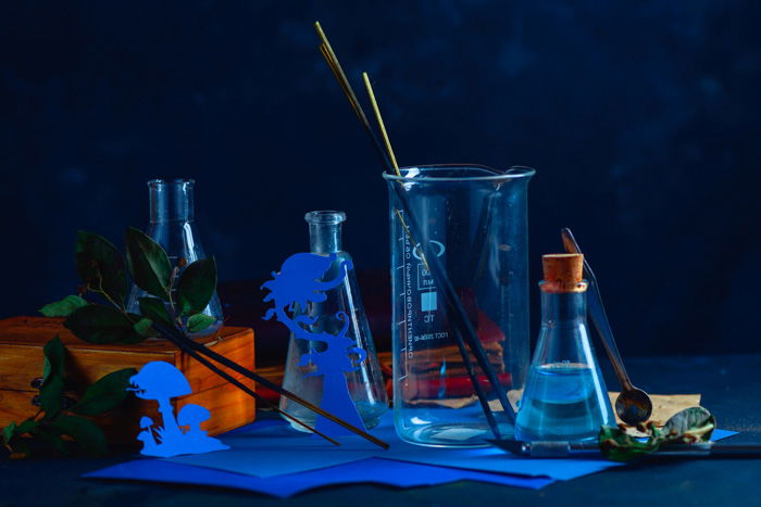 A still life featuring glass bottles ,silhouettes of tiny cut out characters, and incense 