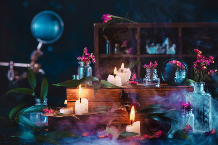 Wizard or witch workplace with burning candles, herbs, vintage wooden boxes and smoke. Dark fantasy still life with blue and orange color scheme