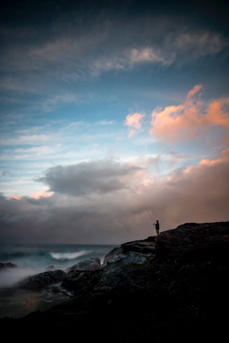 A fisherman fishing off the rocks, landscape shot using orange and blue color scheme