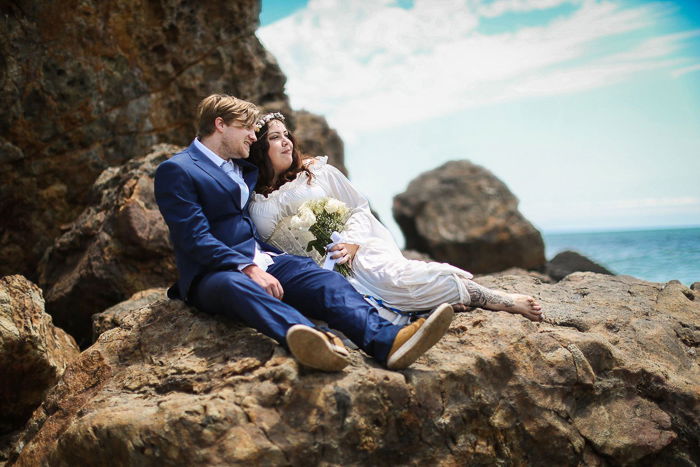 A newly wed couple reclining on rocks at the beach - event photography tips