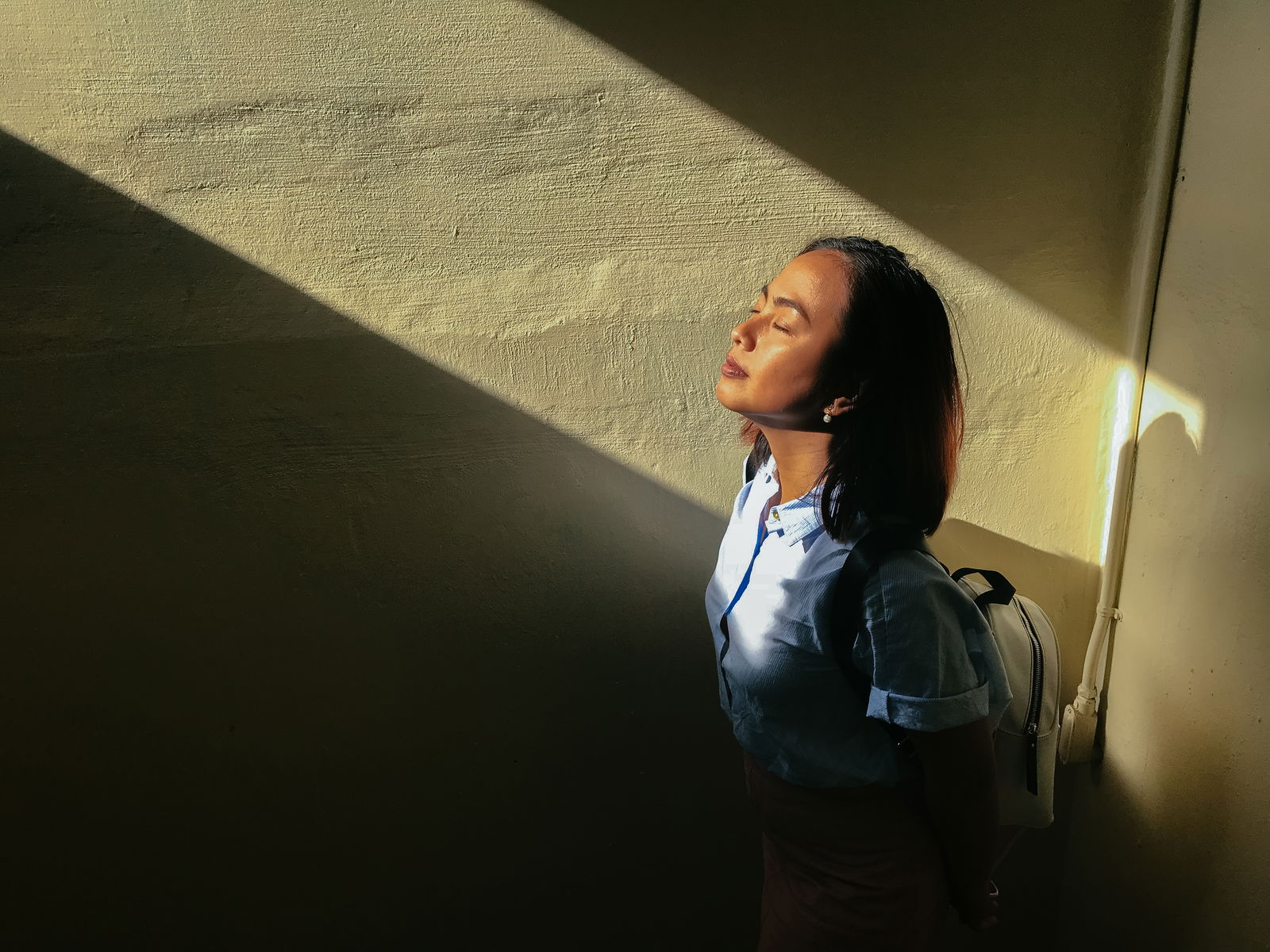 A woman with her eyes closed looking up and being lit by a shaft of sunlight indoors