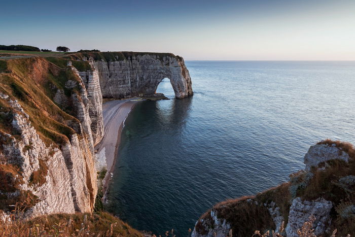 Cliff column jutting out in the blue sea, against a clear softly lit sky