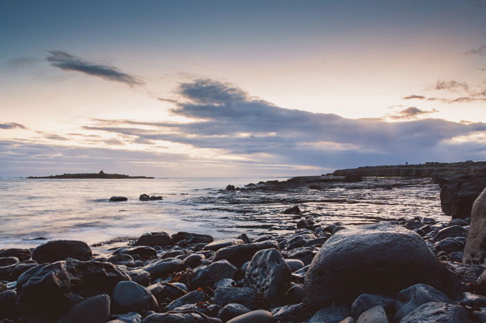 Low vantage point photo of rocks at the coast at sunrise against a cloudy soft lit sunrise