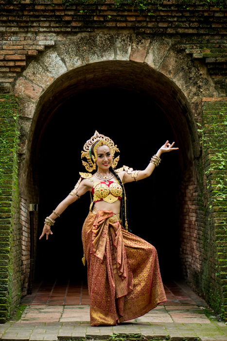 A beautifully costumed smiling thai dancer poses in front of a tunnel - photography composition tips