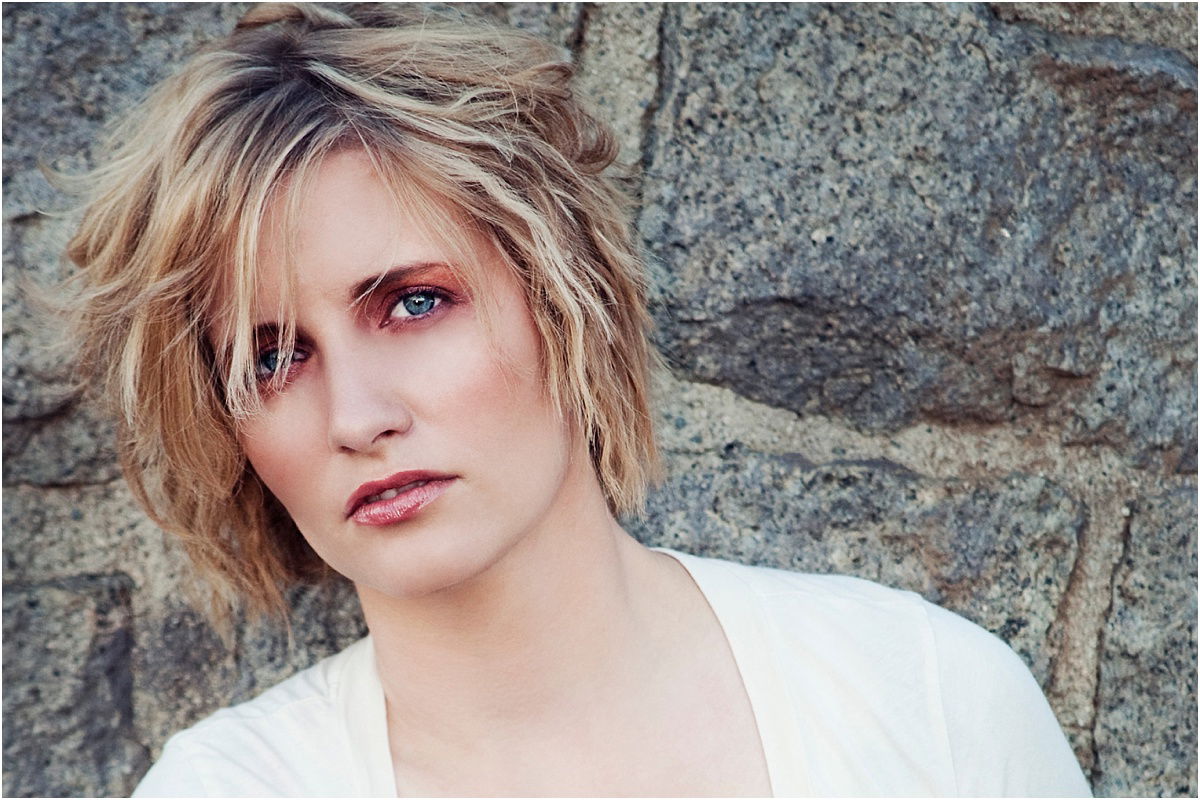 A close-up shot of a woman in makeup with her head titled against a stone backdrop