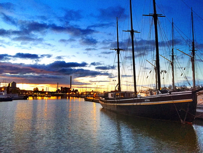 a boat at the harbour, on the blue grey waters, under a deep blue sky, the golden yellow sunset on the horizon - How to Take Stock Photos That Sell