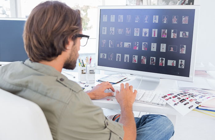 view from behind of a man sitting at his desk viewing several photos on a large computer screen