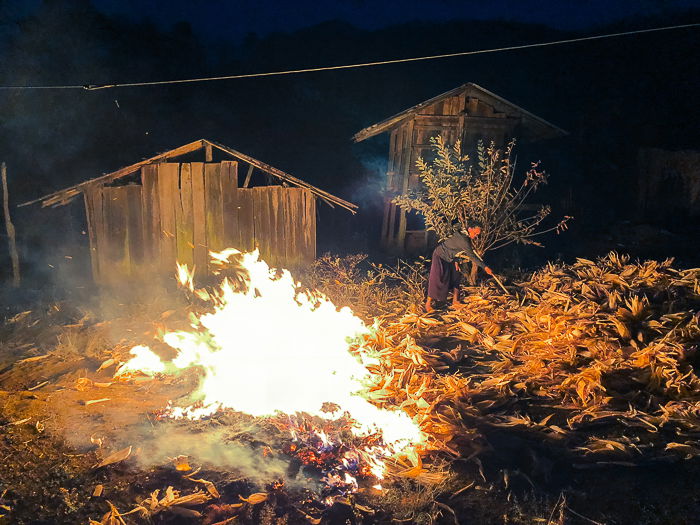 photo of a woman raking leaves into a bonfire near a wood cabin at night