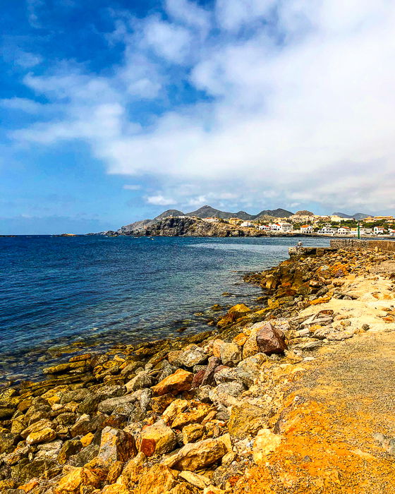 photo of a golden rocky beach, deep blue sea, and cloudy blue sky