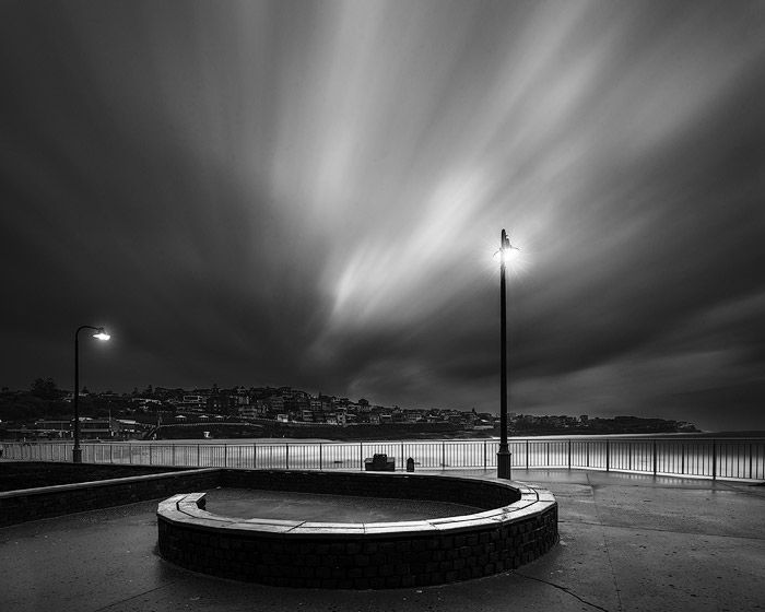 black and white long exposure photo of a seaside lit by lamps at night