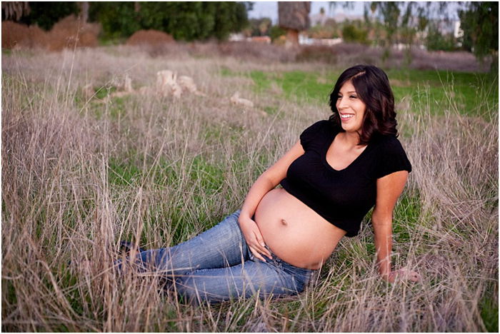 pregnant woman in jeans and a black shirt, sitting in a field