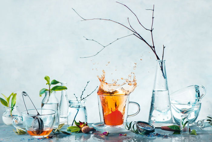 Tea cup with a dynamic splash and glass bottles with green plants and tree branches in a high-key spring still life. Cleanness and freshness concept