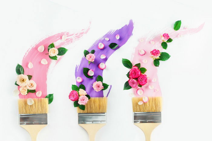 Paintbrushes with paints in pink and violet shades, roses and petals, on a white background. Painting spring creative flat lay. Home decoration concept.