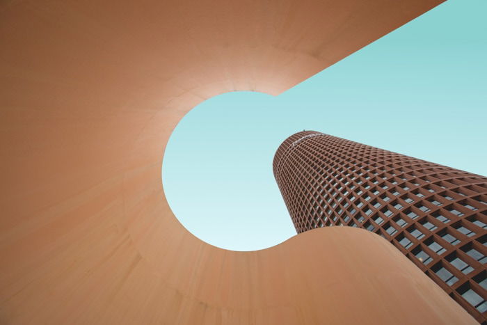 Cool architecture photo looking up through a sculptural element beside a tall multi windowed building 