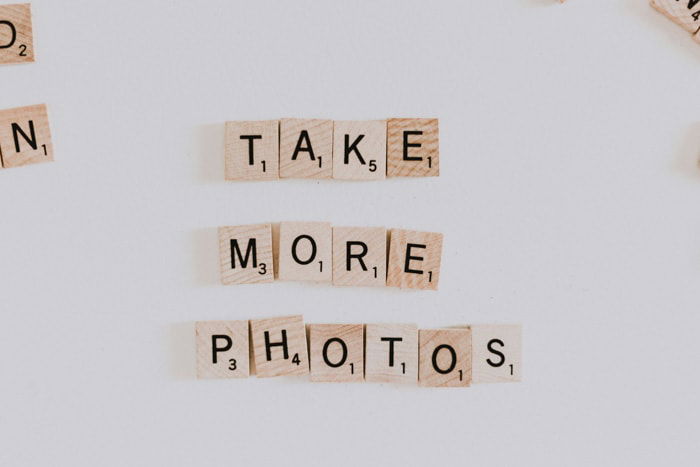 Wooden scrabble pieces spelling 'take more photos' on white background