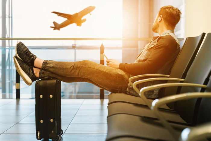 A man sitting in an airport waiting area, watching an airplane ascending from the window