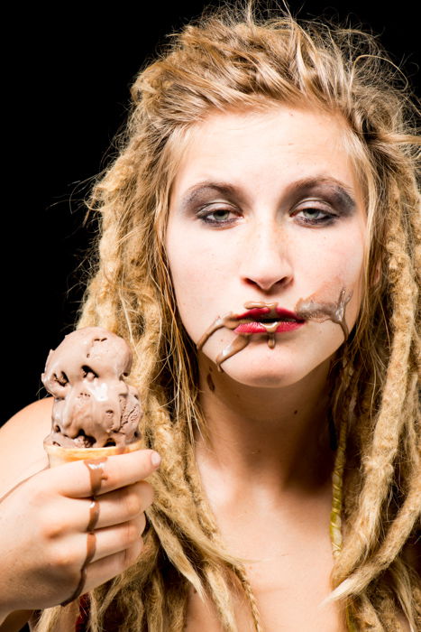 A blond girl with chocolate ice-cream on her face against a black background - photo props