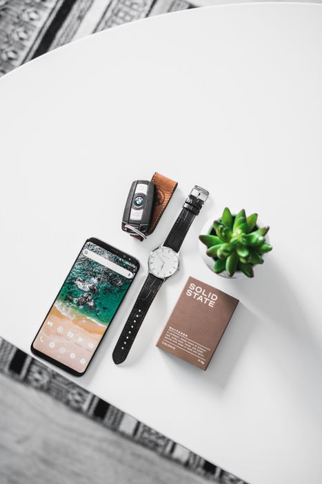 flatlay of man's pocket contents: watch, smartphone, keys, pocket notebook