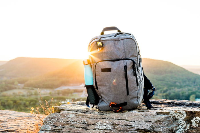 grey backpack sitting on a grey rock outdoors, the sun rising from behind the desert hills on the horizon