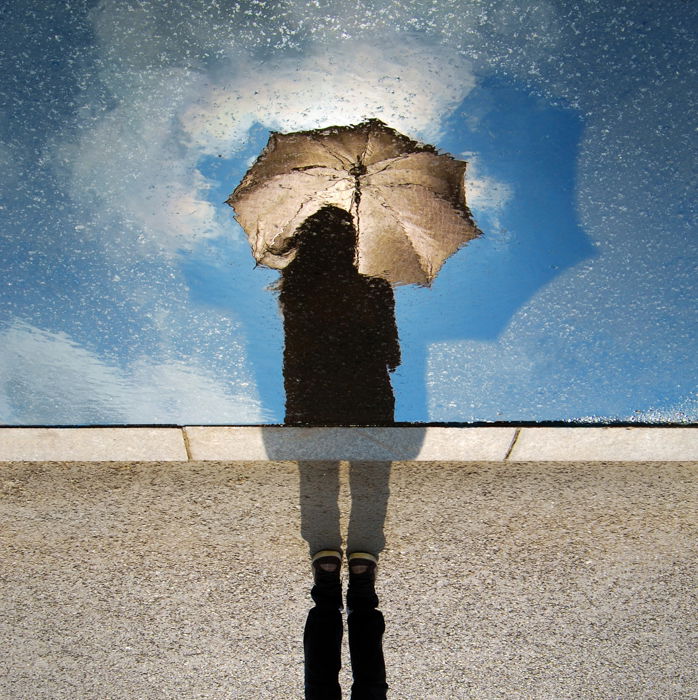 Creative rain photo of a person holding an umbrella, reflected in a rain-splashed window 