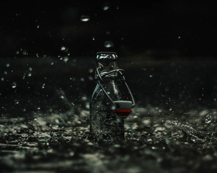 Atmospheric product photography shot of glass bottle splashed with falling rain