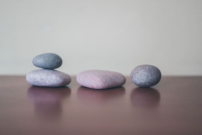 four grey stones on a wooden surface, two stacked, using rule of odds composition