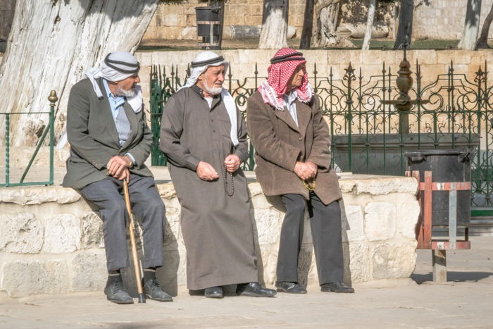 three arab men relaxing sitting by a fountain on a sunny afternoon