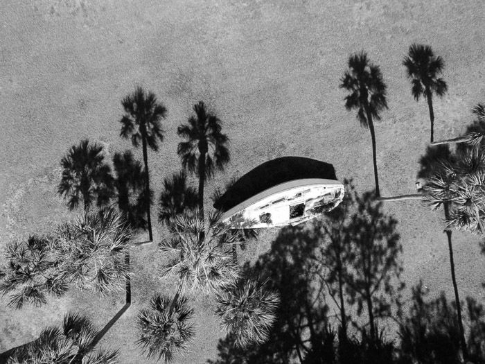 Overhead black and white photo of a wooden boat on a beach surrounded by shadows of palm trees - shadow photography