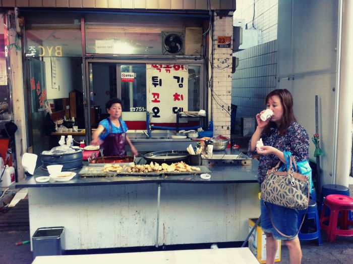 A smartphone street photography shot of a street vendor waiting for a new customer, as a passerby walks past.