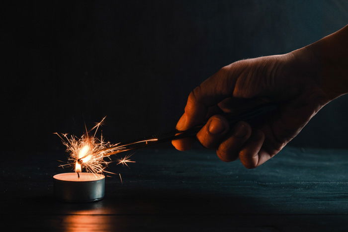 Sparkler photography: hand holding sparkler in a dark room, lighting the sparkler with a tealight candle