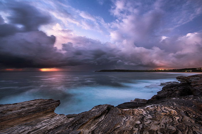 calm waters at a rocky shore, against a purple blue sky, the sunset fading on the horizon. Shutter speed at 30 sec - water photography settings