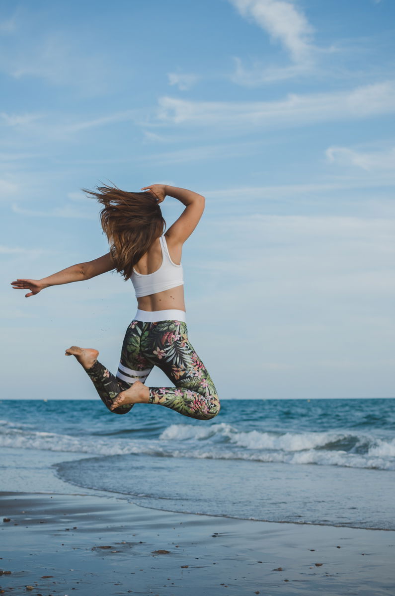 A girl in sports clothes jumping energetically on the beach shot using af mode