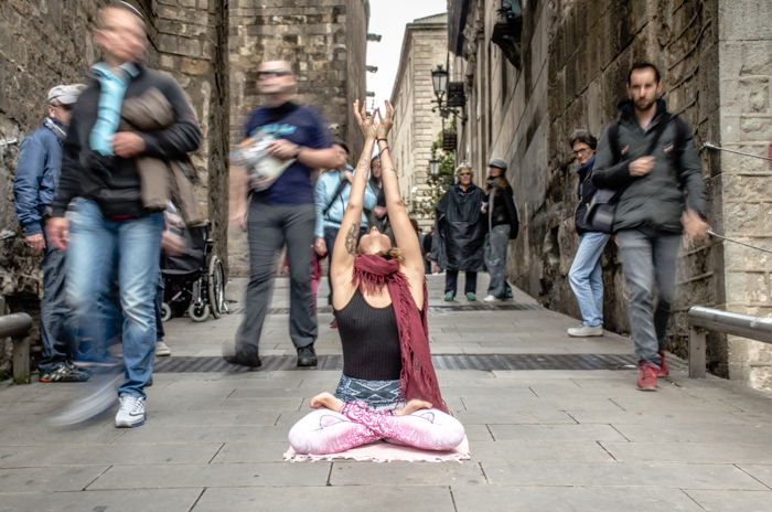 A girl in a yoga pose in the middle of a busy street with blurred pedestrians walking by shot with a slow shutter speed to learn DSLR basics