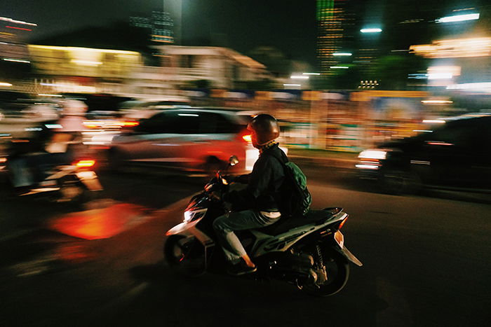 A panning shot of a motorcycle driver with blurred background of moving traffic at night