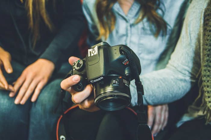 A close up shot of three people looking at A Canon DSLR - strobe light photography