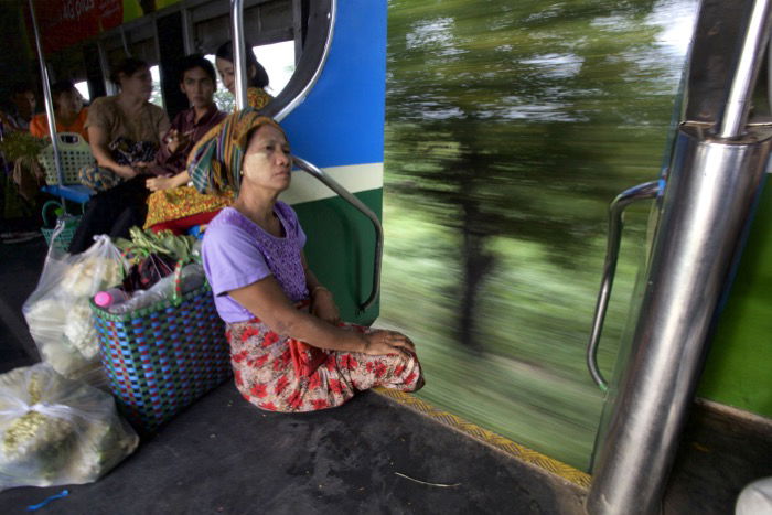 A woman sitting at the edge of a moving train, creative motion blur in the background. Street photography camera settings.