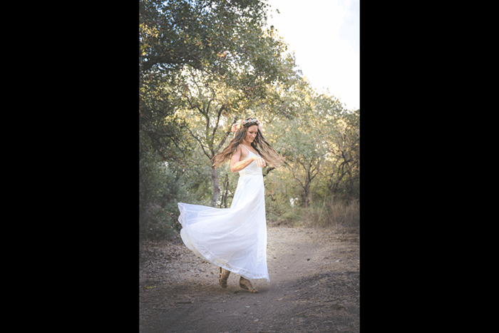 A girl in wedding dress dancing in a forest shot with a fast shutter speed to learn DSLR basics