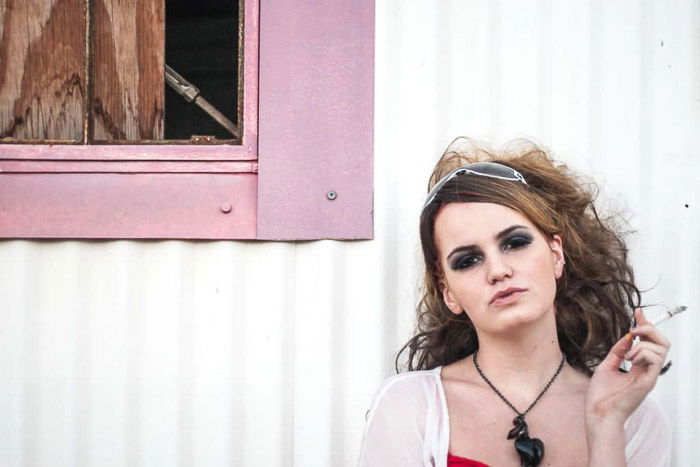 A photoshoot featuring a female model working Time For Print, smoking outside a pink window