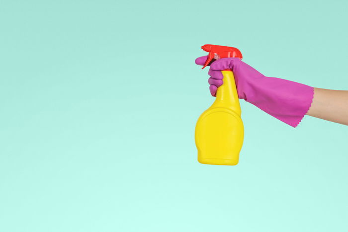 a hand holding a squirt bottle against a teal background