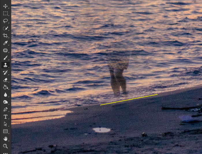 Screenshot showing how to remove something in photoshop, using a photo of a woman walking on a beach at evening time