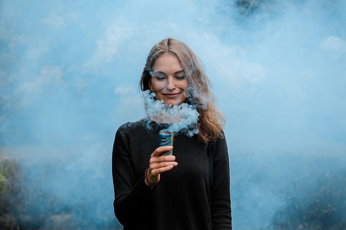 A creative portrait of a woman holding light blue smoke grenade near her face