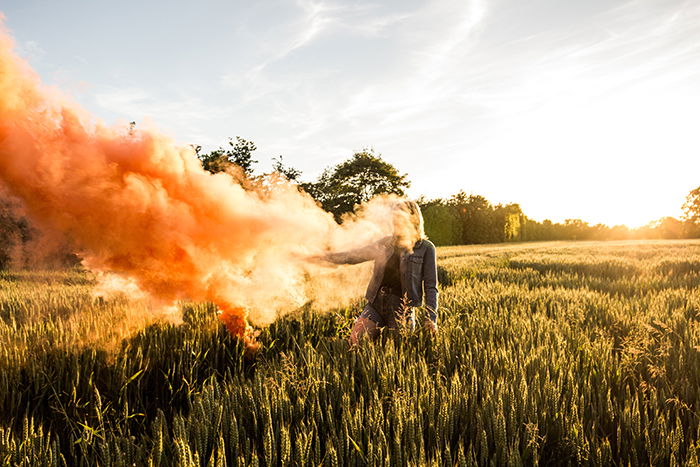 A portrait of a woman holding orange smoke grenades in a cornfield