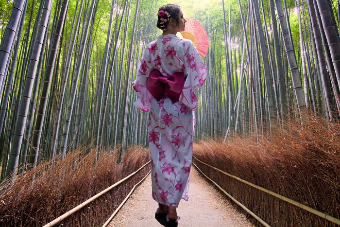 A girl in traditional japanese dress walking through a bamboo forest