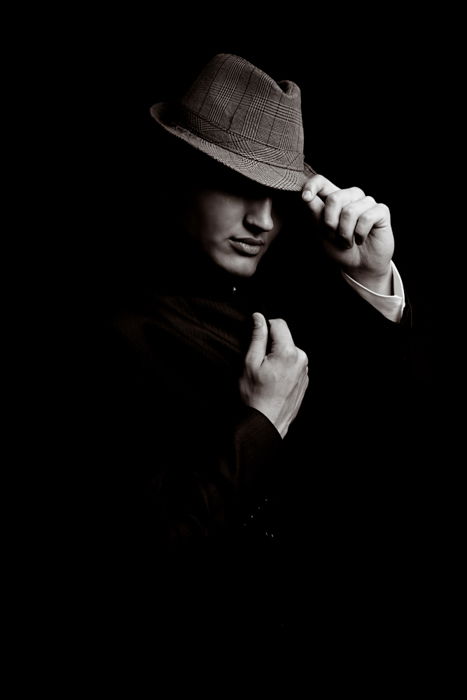 A man in a suit, wearing a fedora hat and posing confidently. 