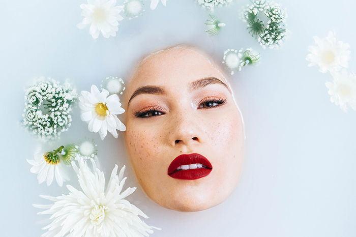 Beautiful milk bath photography of a female model surrounded by white flowers